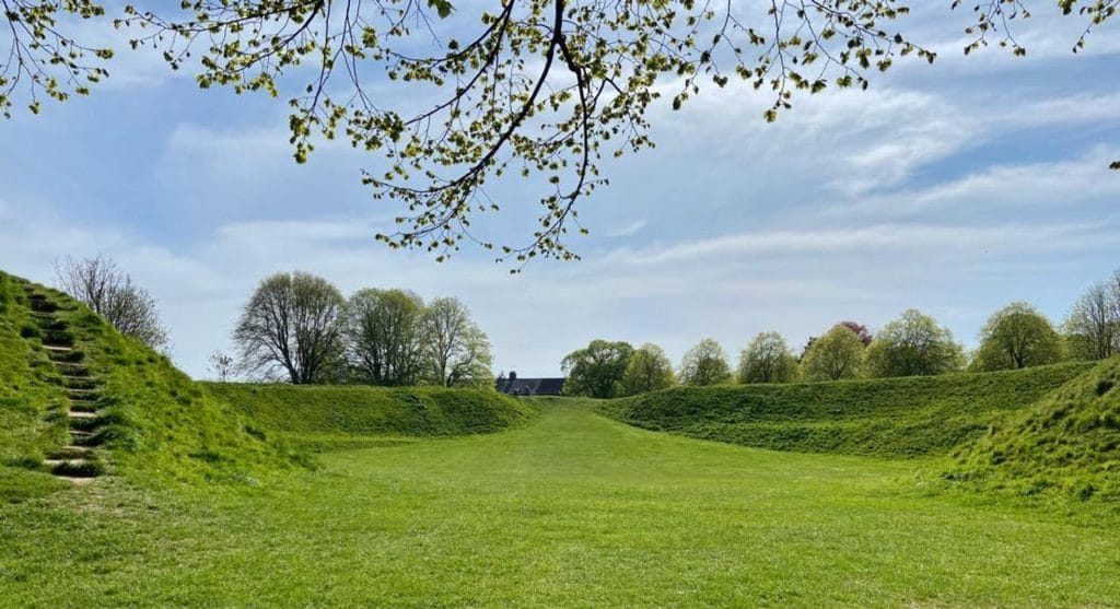 A scenic view of Maumbury Rings with people strolling along the ancient amphitheater's green slopes.