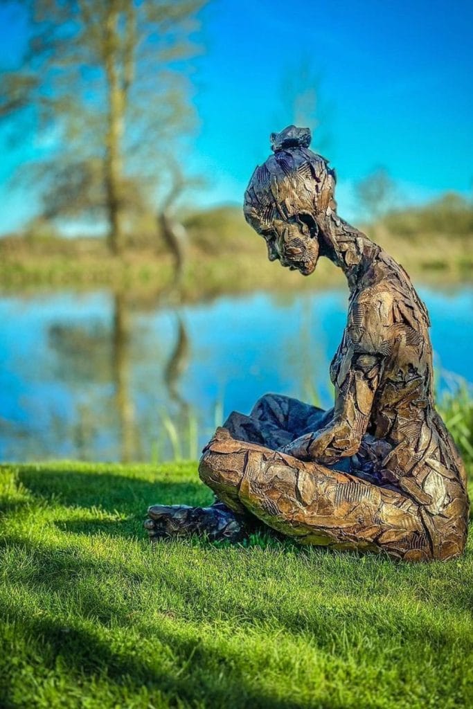 Art sculptures placed by the tranquil lakeside at Sculpture by the Lakes with reflections in the water.